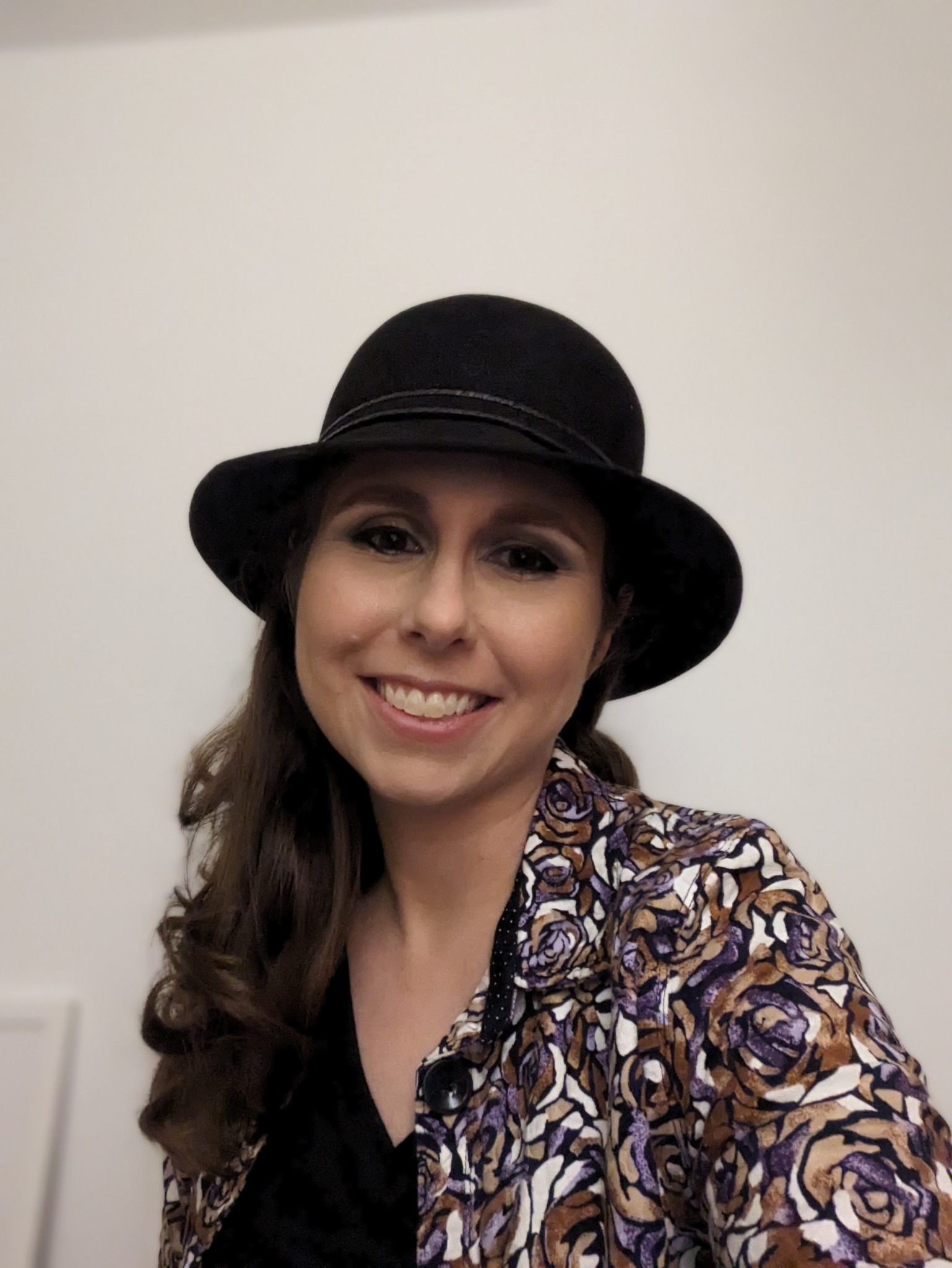 Ragina Fritz smiling in a black hat and floral jacket